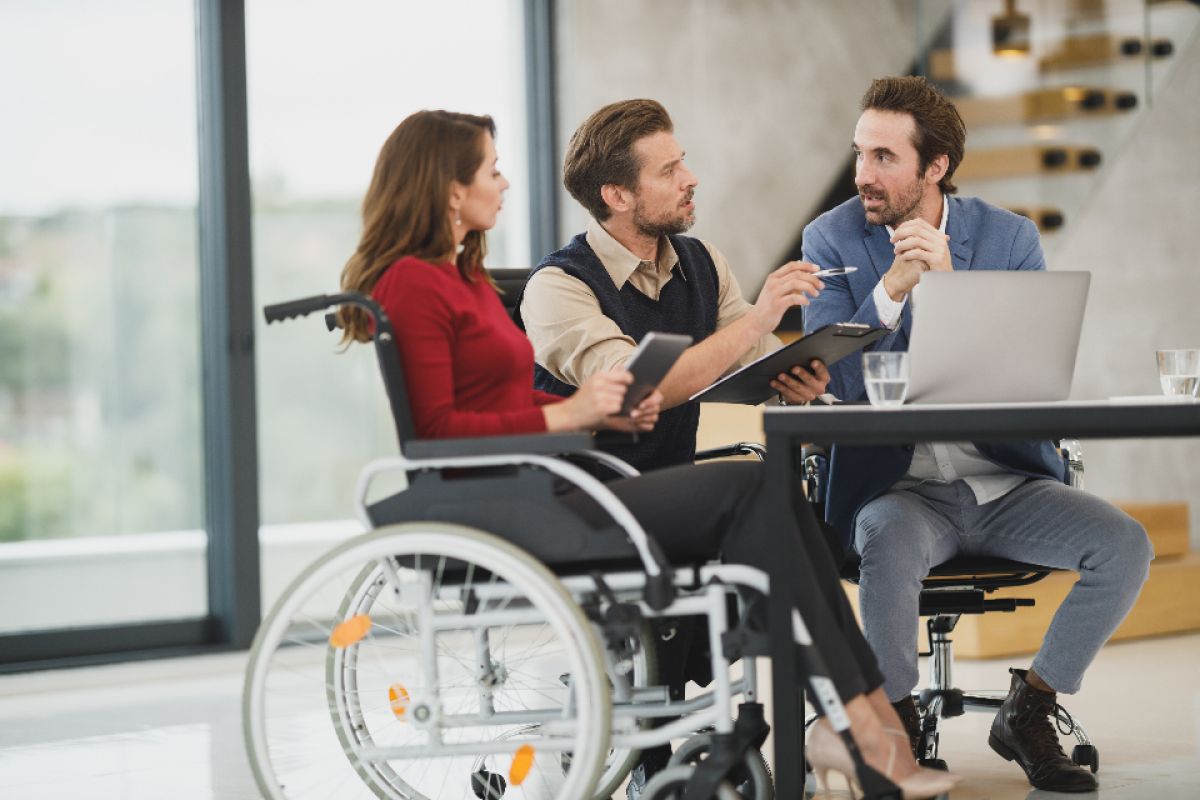 Tre personer som diskuterer iherdig. Den ene personen sitter i rullestol